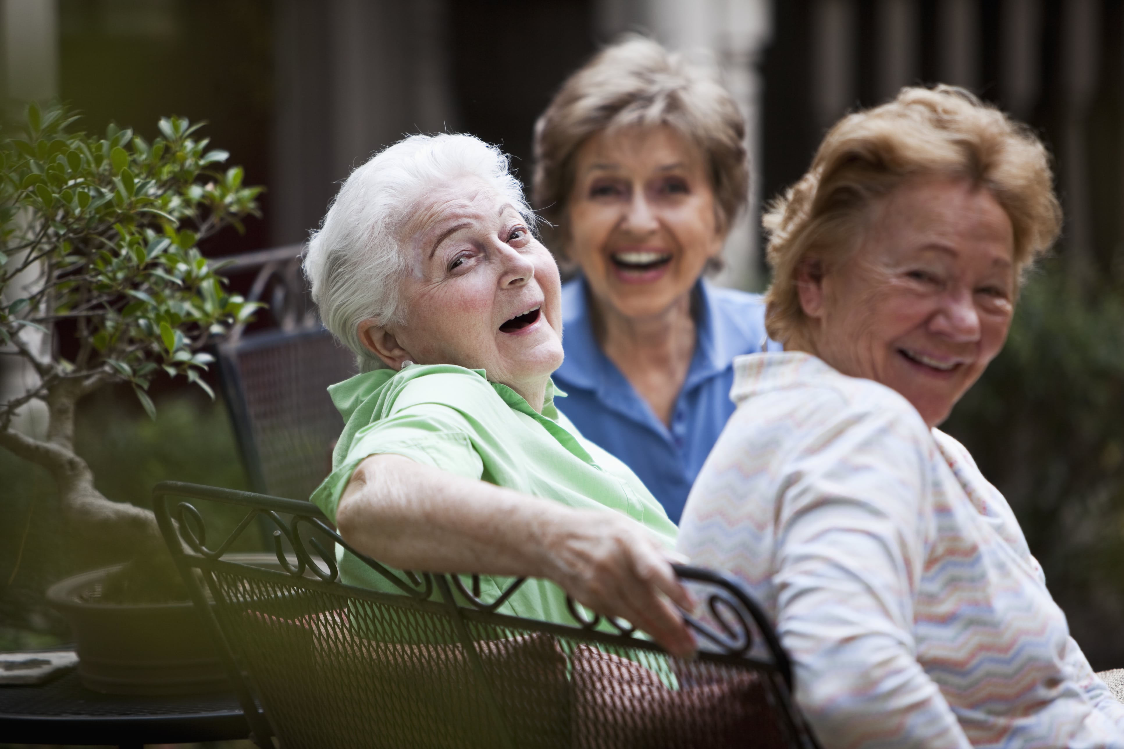 Three older women sitting outdoors, smiling, and enjoying each other.